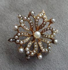 "Yellow gold brooch in the shape of a stylized flower with natural seed pearls and natural half- seed pearls. Brooch is very beautifully shaped with the open, teardrop petals, gracefully curving  from the center pearl to the outside. Each petal is finished with bending to the outside small triangle, having two half pearl, larger placed to the outside, smaller touching the top of the petal. Open in the center, each petal is adorned with ten half-pearls in sizes diminishing to the center. So there Elegant Yellow Gold Baroque Brooches, Elegant Gold Baroque Brooch, Elegant Gold Baroque Brooches, Elegant Baroque Wedding Brooches, Elegant Gold Brooches With Pearl Pendant, Ornate Yellow Gold Wedding Brooch, Yellow Gold Filigree Brooches For Wedding, Wedding Yellow Gold Filigree Brooches, Vintage Gold Pearl Brooches