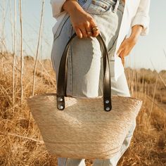 Easily pack up the Jude tote in a suitcase so you can enjoy its versatility with the outfits you've packed for your travels. Its unique shape, with neutral design elements make it the bag that goes with everything. Each handmade basket is unique and may have small imperfections or vary in size and color. All Leah products are responsibly sourced and ethically crafted. Handles: Double layer black leather handles No interior lining Length: 9" Width: 16" Height: 8" Handle Drop: 10" Imported Casual Canvas Straw Bag For Daily Use, Beige Bucket Bag With Top Carry Handle For Travel, Travel Beige Bucket Bag With Top Carry Handle, Travel-friendly Beige Bucket Bag With Top Handle, Casual Natural Shoulder Bag With Top Carry Handle, Casual Beige Bucket Bag With Top Carry Handle, Everyday Summer Tote Bag, Casual Canvas Straw Bag For Everyday Use, Casual Beige Shoulder Weekender Bag