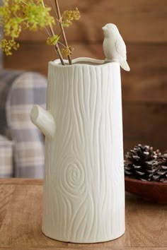 a white vase sitting on top of a wooden table next to a pine cone and plant