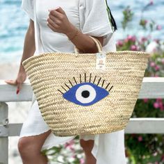 Introducing the Straw Evil Eye Large Bag: Your Perfect Summer Companion Embrace the spirit of summer with our stunning Straw Evil Eye Large Bag. This handcrafted accessory combines traditional craftsmanship with trendy design, making it the ideal choice for beach outings, picnics, or casual city strolls. Exquisite Handmade Craftsmanship Each Straw Evil Eye Large Bag is meticulously handcrafted by skilled artisans, ensuring that every piece is unique and of the highest quality. The natural straw White Bohemian Beach Bag For Summer, Palm Leaf Beach Bag For Travel And Beach Season, Coastal Style Natural Color Bags For Vacation, Natural Color Coastal Style Vacation Bag, Natural Handwoven Straw Bag For Summer Outings, Embroidered Natural Straw Beach Bag, Blue Handwoven Summer Beach Bag, Embroidered Natural Straw Bag For Beach, Bohemian Straw Bag For Beach Season Vacation