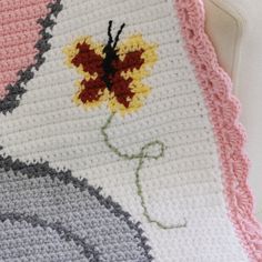 a crocheted blanket with a flower on it is shown in pink, gray and yellow