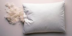 a white pillow sitting on top of a white wall next to a pile of feathers