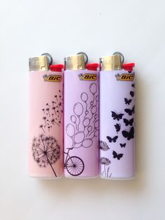 three lighters with designs on them are lined up against a white wall and one has a dandelion in the middle