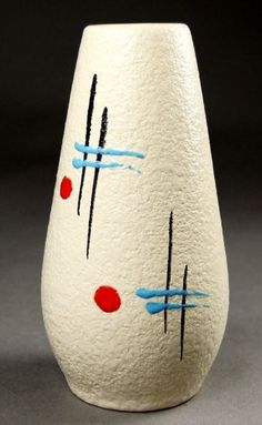 a white vase with blue and red designs on it's sides, sitting on a gray surface