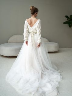 a woman in a white wedding dress is standing near a couch and looking down at the floor