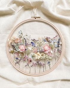 the embroidery is being worked on with white thread and pink and blue flowers in it