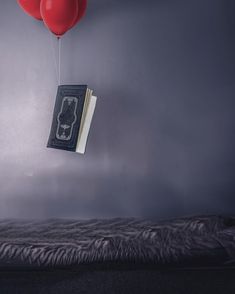 two red balloons floating over a bed with a book hanging from the ceiling above it