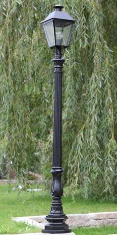 an old fashioned lamp post in the middle of a park with trees and grass behind it