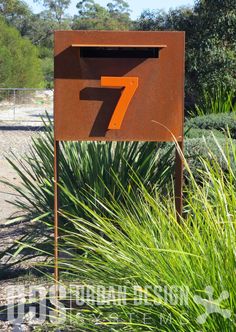 the number seven sign is in front of some tall grass and bushes with trees behind it