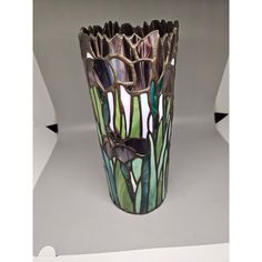 a glass vase with flowers and leaves on it's sides, sitting on a white surface