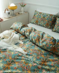 a bed with blue and orange floral bedspread, white pillows and a yellow lamp