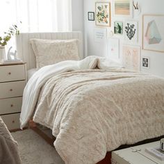 a bedroom with white walls and pictures on the wall above the bed, along with a beige comforter