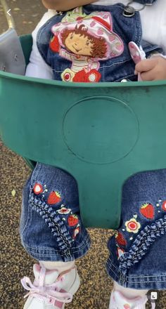 a baby doll sitting in a green plastic toy wagon on the ground with its legs crossed