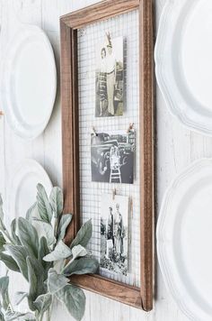 a wooden frame with pictures hanging on the wall next to plates and a potted plant