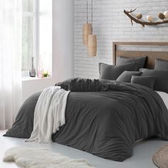 a bed with grey sheets and pillows in a room next to a brick wall,