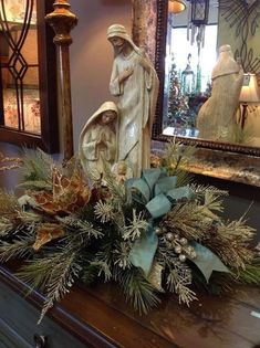 a christmas arrangement on top of a dresser with a statue and mirror in the background