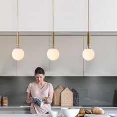 a woman sitting on the kitchen counter reading a book while holding a bowl and spoon