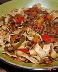 a green plate topped with pasta and meat covered in sauce on top of a wooden table