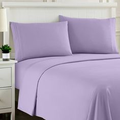 a bed with purple sheets and pillows on top of it, next to a night stand