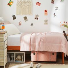 a bed with pink sheets and pillows in a bedroom next to a white wall filled with pictures