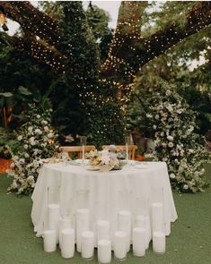 a table with white candles and flowers on it in the middle of a green field