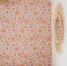 a wall with a flower pattern on it next to a mirror and wicker basket