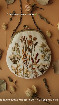 a white purse with flowers on it sitting on a table next to leaves and branches