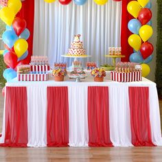 a table topped with cake and balloons next to a white table covered in red curtains