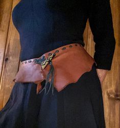 a woman wearing a belt with leather and metal decorations on the waist, standing in front of a wooden wall