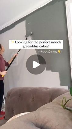 a woman is using a paint roller to paint the walls in her living room with grey and white colors