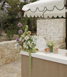 an outdoor bar with flowers and candles on the outside wall, next to a white umbrella