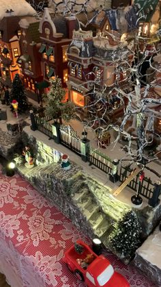 a red car is parked in front of a christmas village with lights and snow on the ground