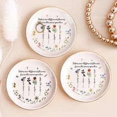 three plates with flowers on them sitting next to a beaded bracelet and necklaces