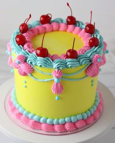 a yellow cake with pink, blue and green frosting topped with cherry cherries