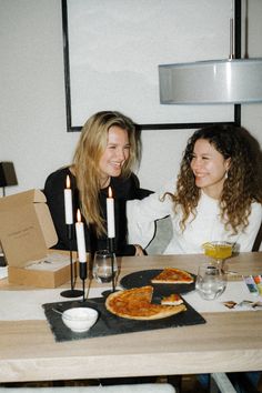 two women sitting at a table with pizza and drinks