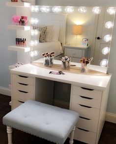 a white vanity with lights on it and a stool