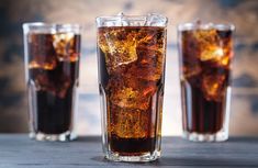 two glasses filled with soda sitting on top of a table