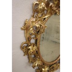 an ornate gold mirror hanging on the wall next to a white wall with flowers and leaves