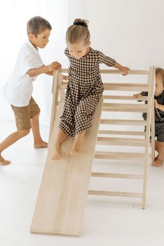 two children playing on a wooden slide in a room with white walls and flooring