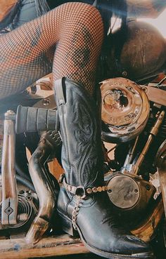 a woman sitting on top of a motorcycle with her legs in the air and wearing boots