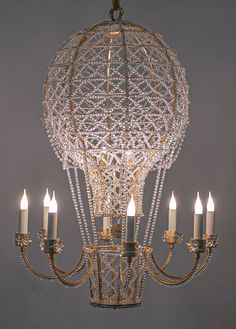 a chandelier with five lit candles hanging from it's center, in front of a gray background