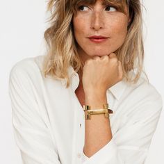 a woman wearing a white shirt and gold bracelet with her hand resting on her chin