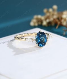 a blue stone ring sitting on top of a white card next to some dried flowers