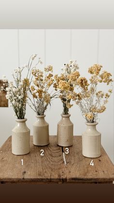 four vases with flowers in them sitting on a wooden table next to each other