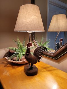 a rooster lamp sitting on top of a wooden table next to a mirror and potted plant