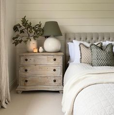 a white bed sitting next to a wooden dresser with a lamp on top of it