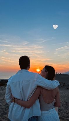 a man and woman standing on top of a sandy beach under a heart shaped kite