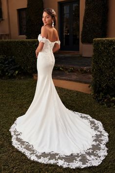 a woman in a white wedding dress standing on the grass with her back to the camera