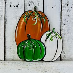 three painted pumpkins sitting on top of a white wooden wall next to each other