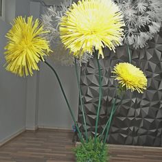 three yellow dandelions in a vase on a wooden floor next to a wall